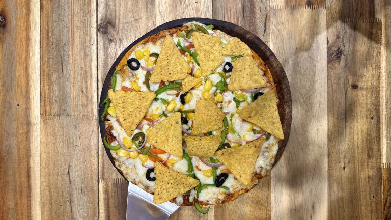 Pizza with corn, tortilla chips, olives, and peppers on a wooden table