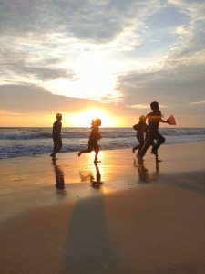 Children at Kozhikode Beach joyfully play in the warm golden glow of the sunset, casting long shadows on the waves, creating a serene scene of joy and freedom.