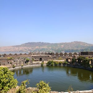 Inside the walls of the Murud-Janjira fort, including a large, deep pool of water. Hills and the sea are in the background.