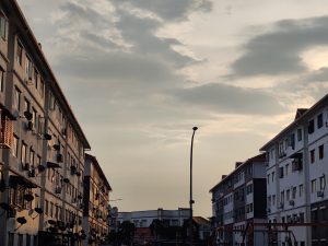 Twilight sky above a row of urban residential buildings with satellite dishes and a street lamp in the foreground.