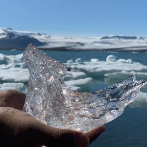 A fleeting moment of frozen beauty: A hand holding a transparent piece of ice on the bank of a river.