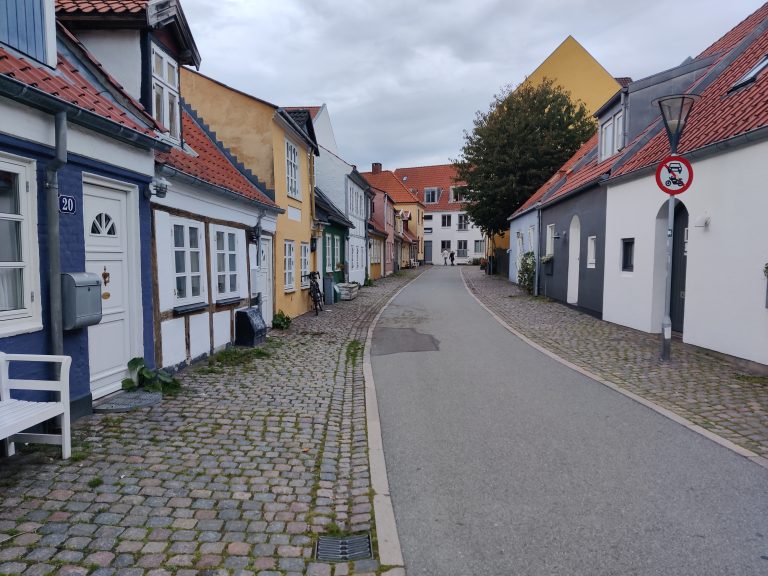 Cobbled street winding between colorful traditional houses with a no entry sign for vehicles in Aalborg Denmark.