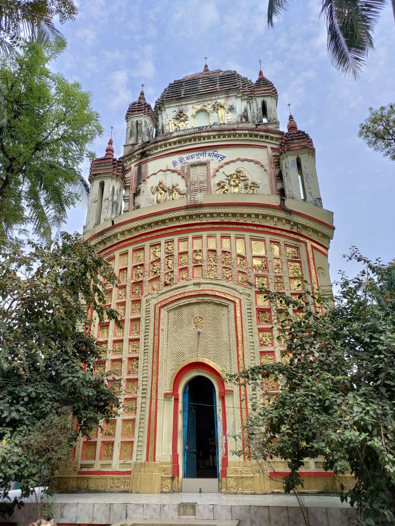 The entrance of a temple, the temple has many golden mini statues on it. On the left and the right of the entrance there are trees.