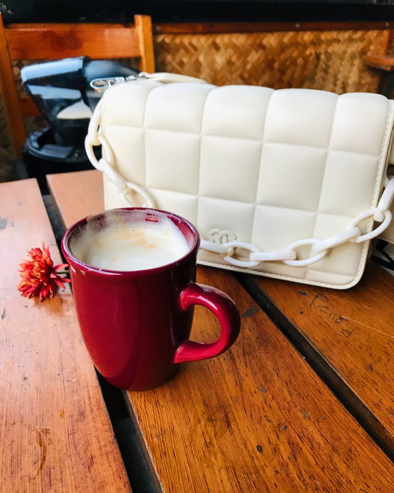 A cup of tea in a small red cup and a white ladies’ bag in the background.