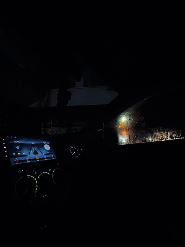 The dashboard of a car at night with rain pouring down the window