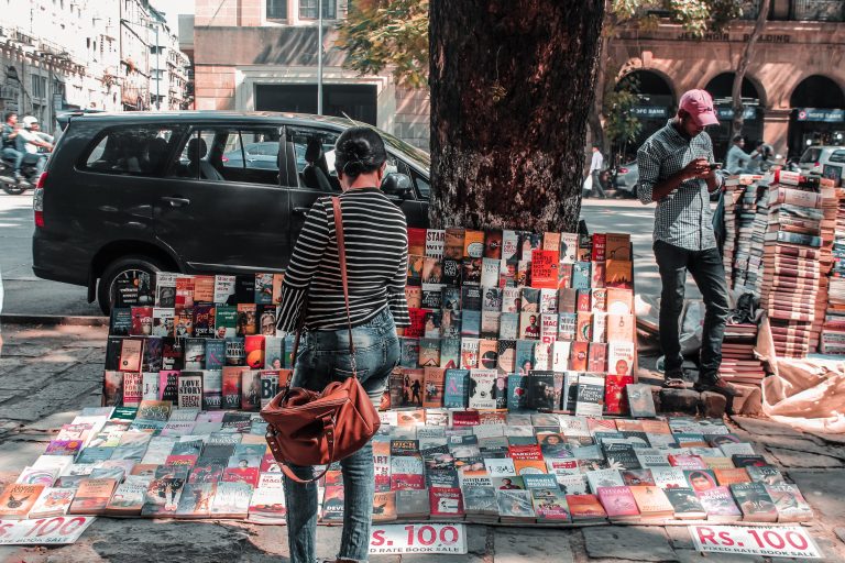 Image of a roadside bookstall with books and customers browsing them.