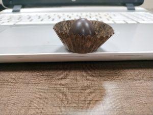 A chocolate candy in a brown paper sitting on a laptop
