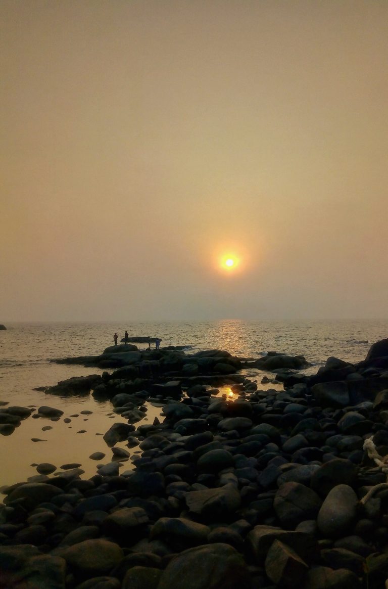 people are watching sunset on a rocky beach, and the sun casting a final burst of golden light before surrendering to the night