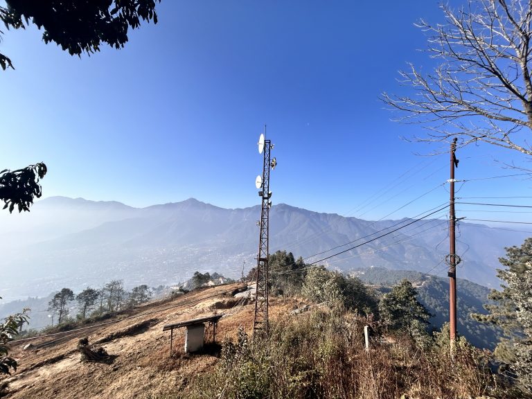 A transmission tower on a tree scattered hill, hazy mountain vista