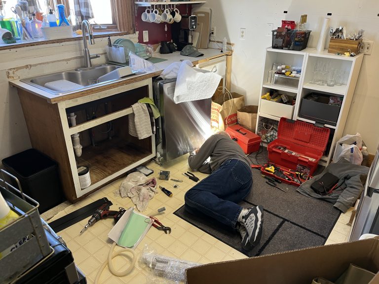 Man lying on kitchen floor surrounded by tools installing a dish washer