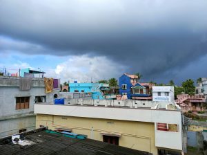 The dark clouds forming before cyclone appears in a street with colourful buildings.
