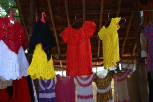 Colorful woollen crocheted garments hang from lines below a bamboo cane frame roof of a shop in Shilpgram, Udaipur.