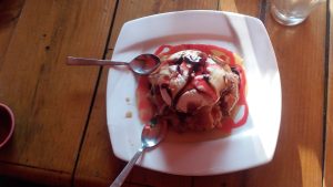 A tasty ice cream cake is displayed on a white plate, with two spoons nearby.