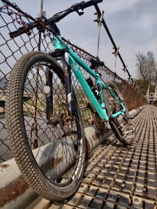 A green bicycle leans against the wire fence on a bridge over the water
