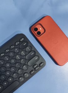 Partial view of a black keyboard beside a red iPhone on a blue surface
