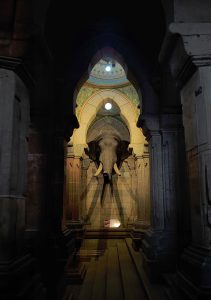 Looking down a hall through columns at an Elephant head sculpture at mysore palace, Karnataka.