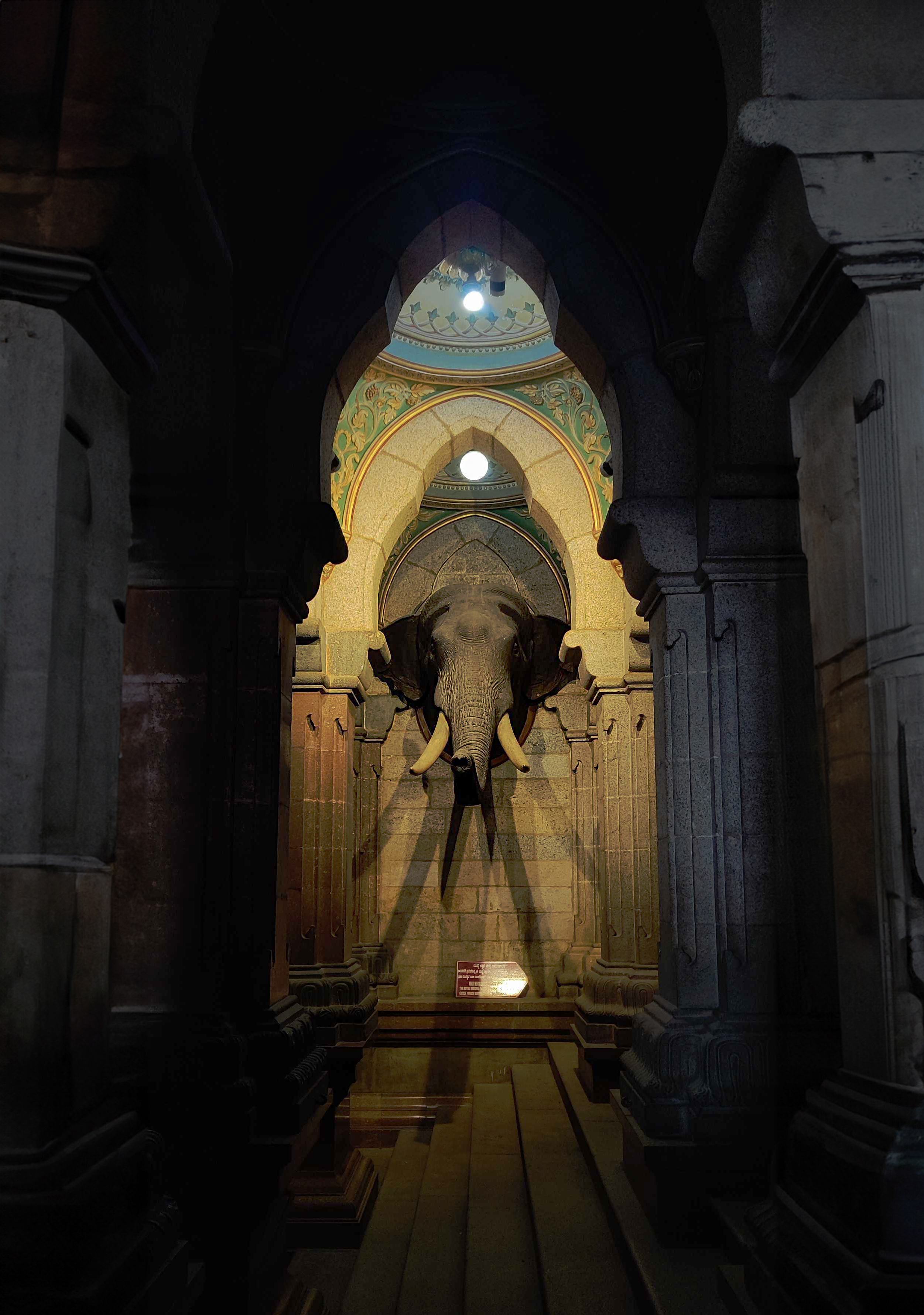 Looking down a hall through columns at an Elephant head sculpture at mysore palace, Karnataka.