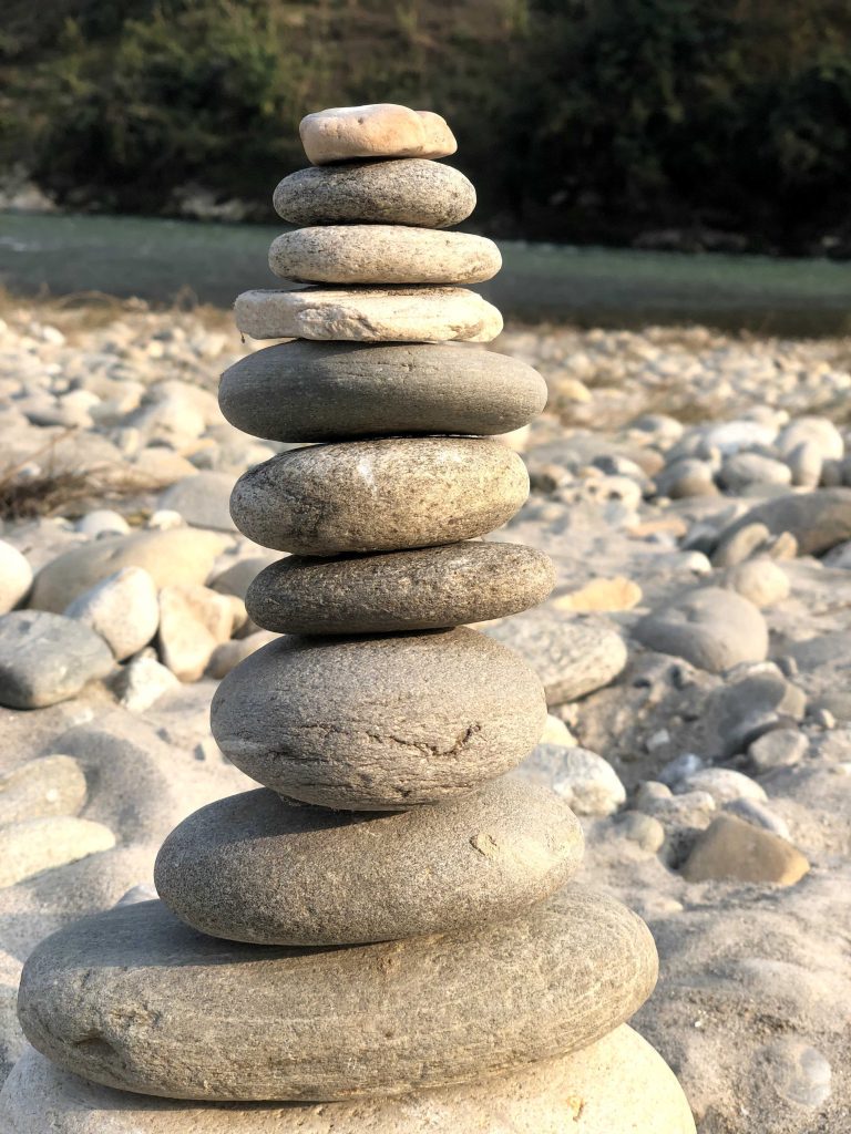 Stack of smooth, round stones balanced on a pebble-covered riverbed in daylight.