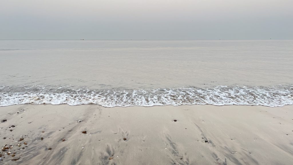 A sandy beach with a wave coming in to shore.