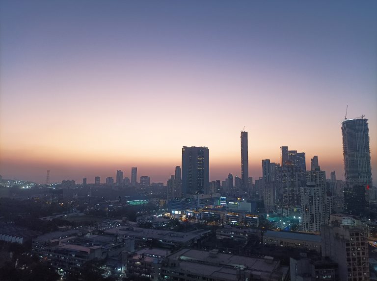 A Mumbai city skyline during twilight with various high-rise buildings and a gradient of pink to blue colors in the sky.