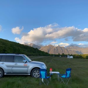 Iceland chill zone: Car parked on a lawn with chairs and a desk besides it with a beautiful view of mountain ranges in the background. 