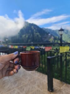 A hand holding a tea cup. Mountains and prayer flags in the background.