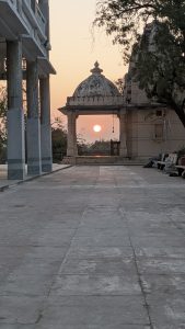 The image features a stone walkway leading up to a domed building. In the background, The photo was taken at a Hindu Temple during a sunrise.