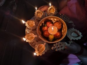 Person holding a brass plate with lit oil lamps (diyas) and flowers during a traditional Hindu ritual, symbolizing spirituality and peace.