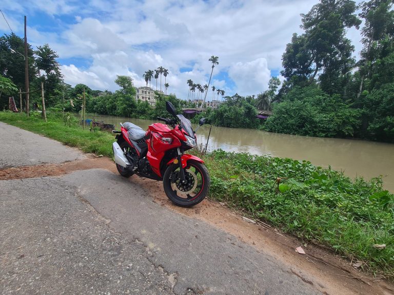 Red motorcycle parked by a river road: Vibrant bike against a scenic backdrop, riverside tranquility.