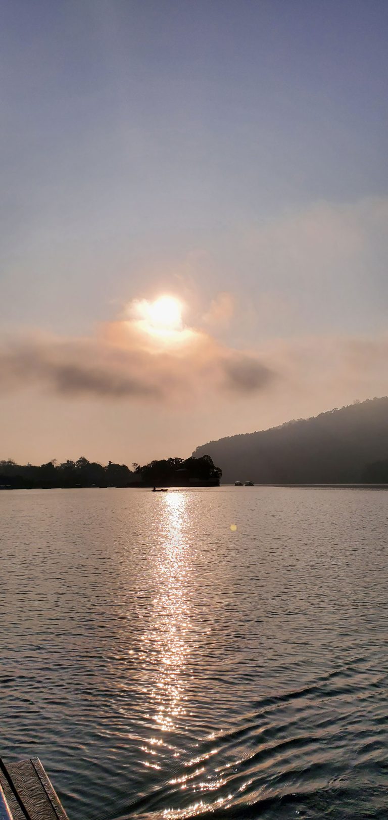 Fewa Lake reflects the sun’s golden light while clouds obscure the sun.