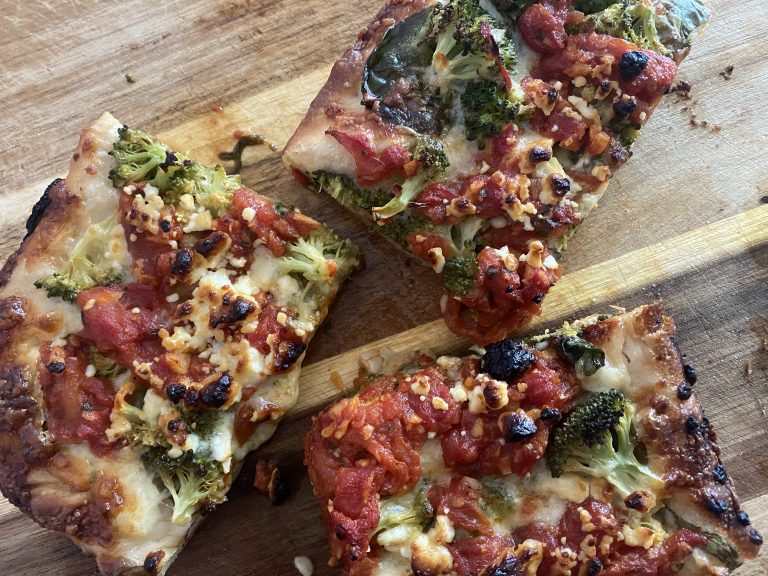 Three pieces of a broccoli, spinach, garlic, and tomato Sicilian style pizza on a cutting board