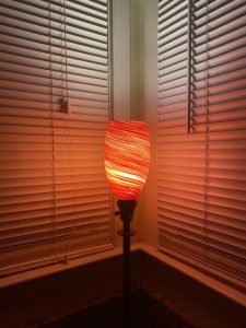 red swirled glass table top light fixture in the corner of two windows with the blinds closed
