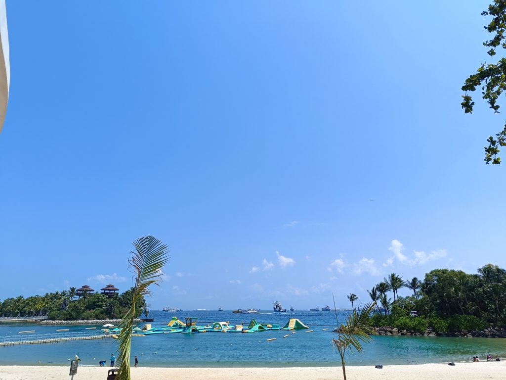 Tropical paradise on Sentosa Island, Singapore, featuring sandy beach, palm trees, and azure water.