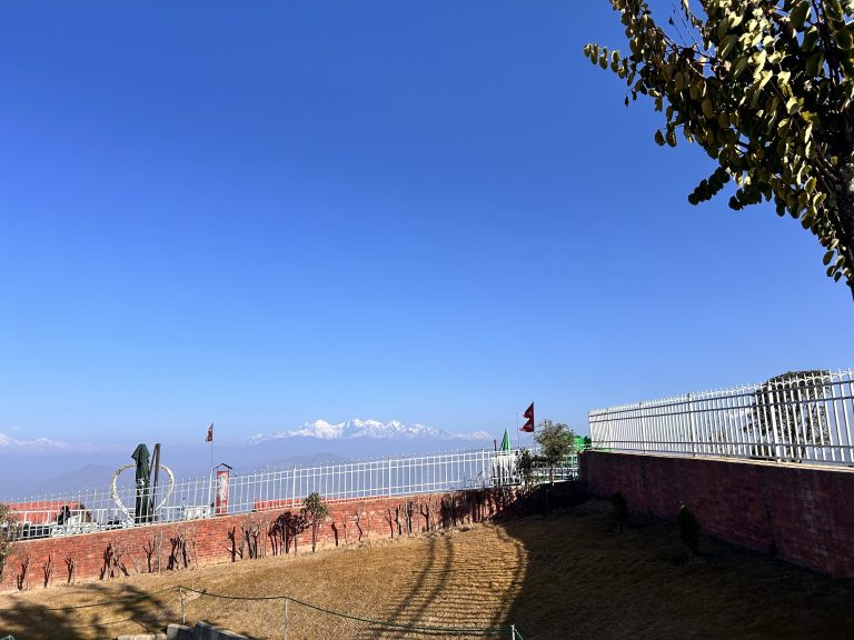 Snow-capped Himalayan vista, brick wall, fence railings and flags fly in the foreground