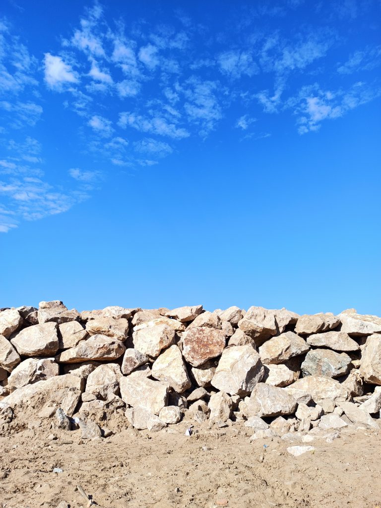 The sky is a bright shade of blue with white clouds scattered across it over a stone wall and sandy ground.