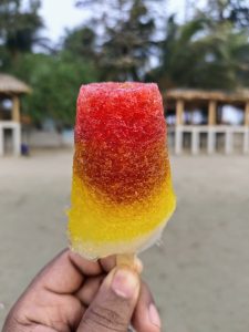 A colorful lolly ice cream in hand on a beach.