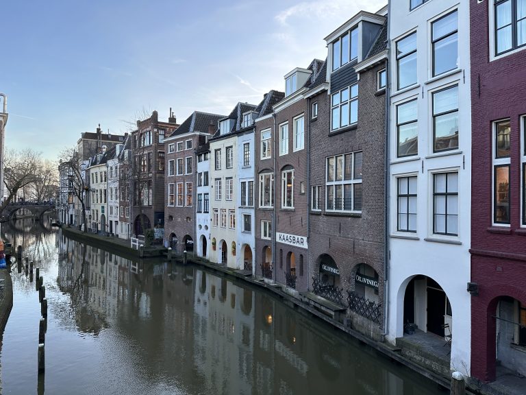 Several buildings of different colors (red, brown, white, beige), all facing the canal in a Dutch city – Utrecht.