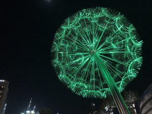 A sculpture resembling a dried dandelion illuminated with green light