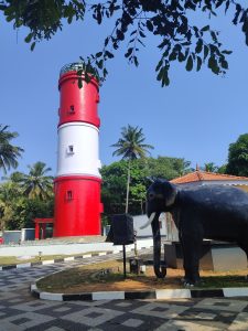 A red and white lighthouse with a statue of an elephant in the foreground
