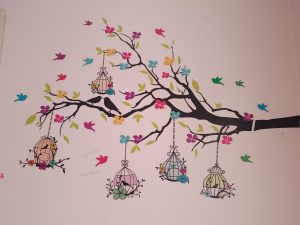 A wall painting contains, tree, flowers, birds and nests. 