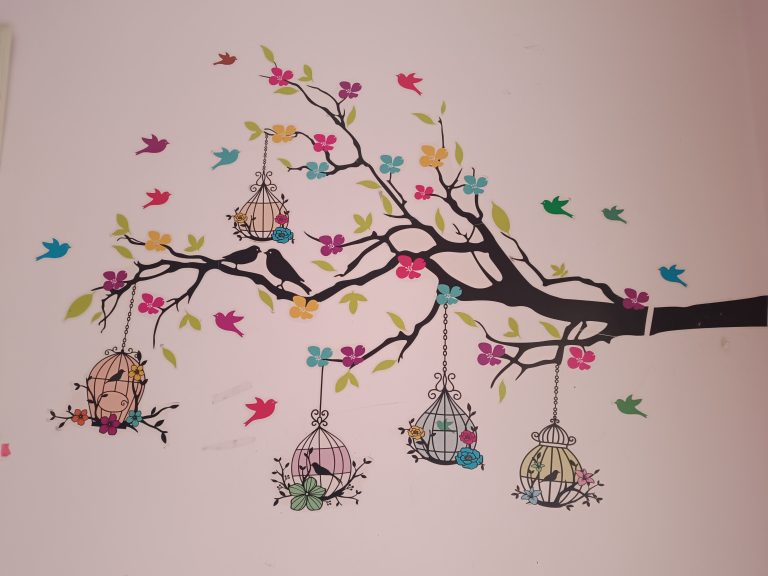 A wall painting contains, tree, flowers, birds and nests.