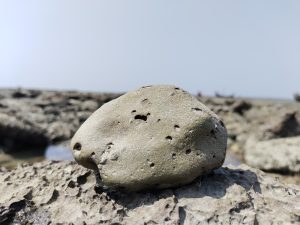 A small rock stand on a big rock at beach.