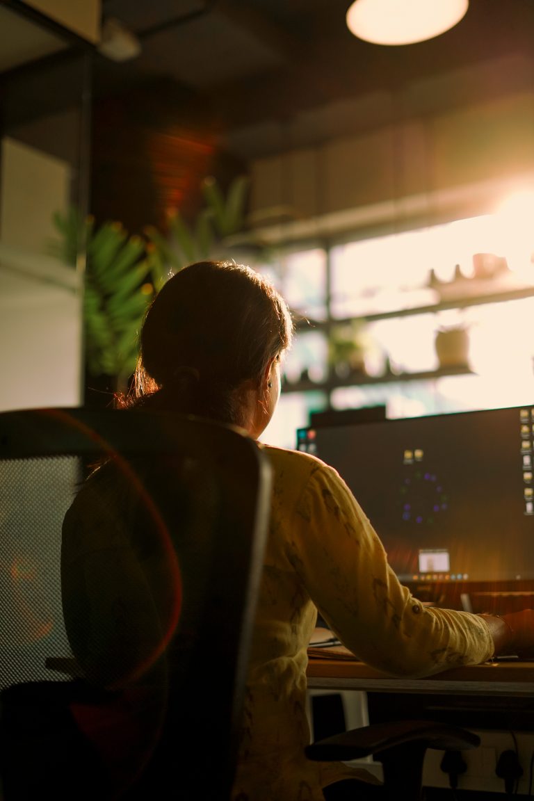 A girl working on a computer system near a window with sunlight is shining through it.