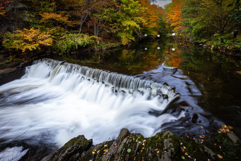 A long exposure of a small waterfall with trees changing colors all around it.