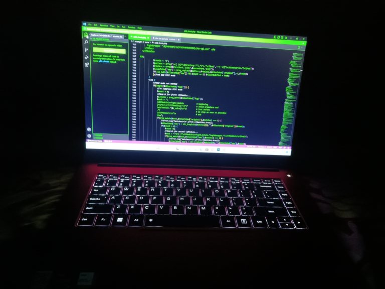 A laptop with illuminated keyboard and green texts on the screen in a dark room.