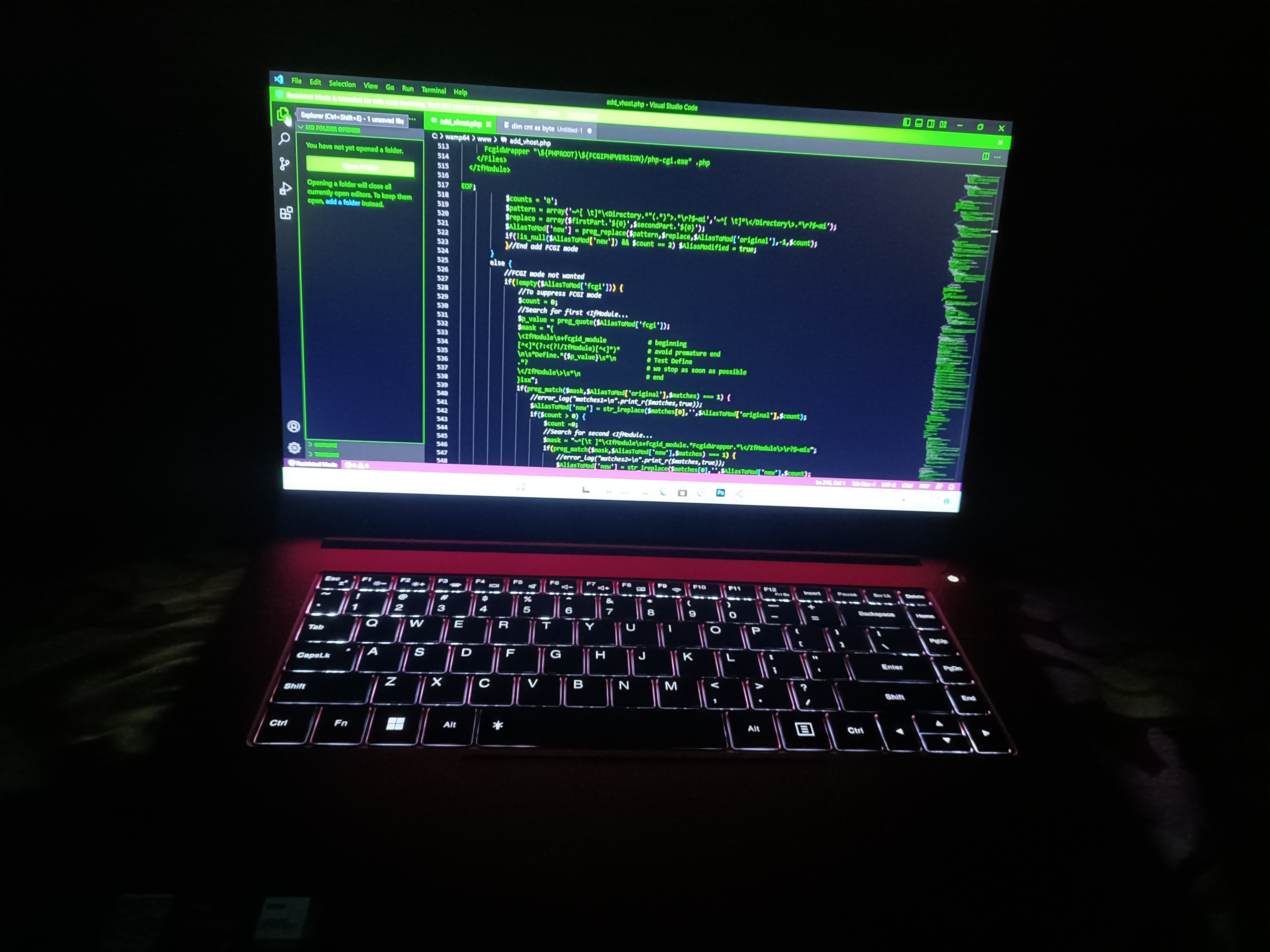 A laptop with illuminated keyboard and green texts on the screen in a dark room.
