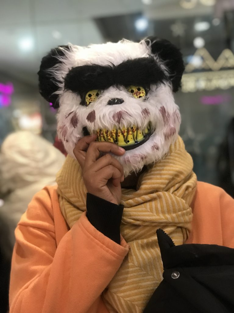 A person holds a scary panda mask in front of their face