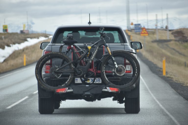 Suv car on the road with a bicycle attached to the back of it.