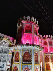 Highly decorative, patterned building adorned with flowers and lights against the night sky. Electricity cables run overhead.