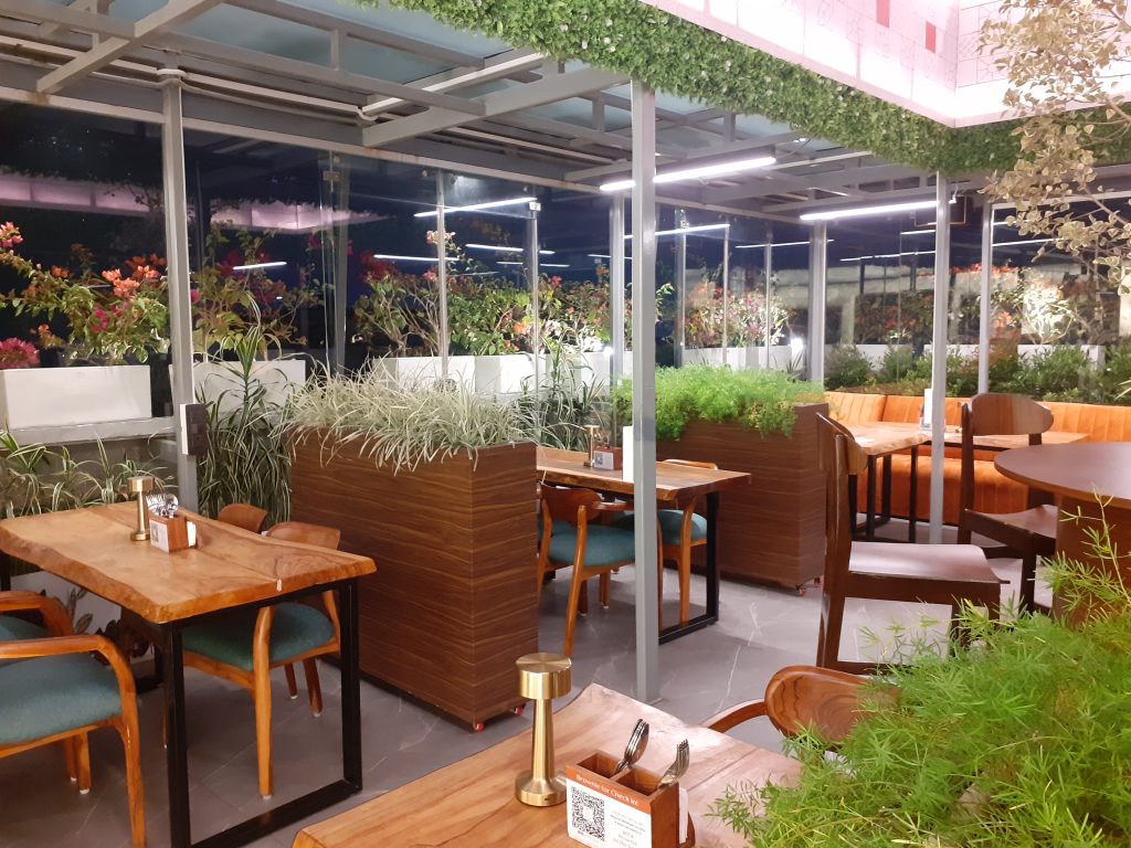 A cafeteria in Kolkata with. plants and bushes around the table.